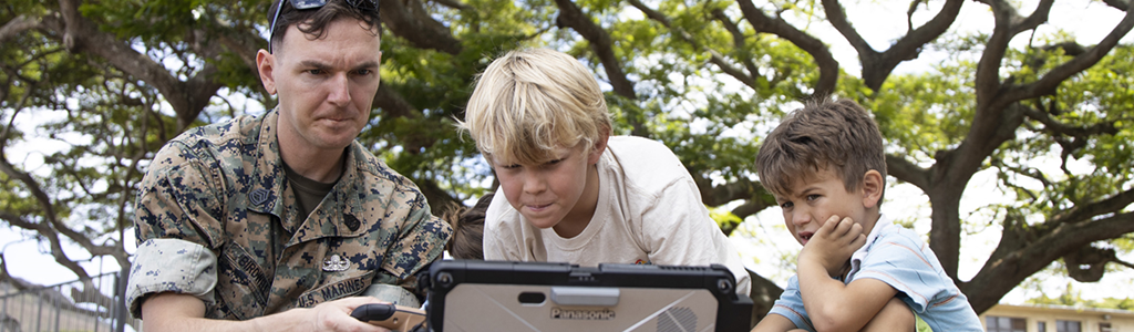 Marine showing robotics on laptop to children